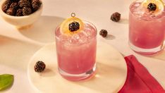 two glasses filled with pink lemonade and blackberries on top of a white plate