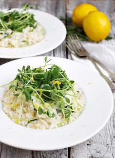 two white plates filled with rice and vegetables on top of a wooden table next to lemons