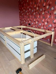 an unfinished bed frame with drawers and tools on the floor in front of a floral wallpaper