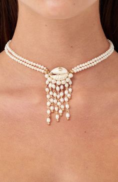 A central cowrie shell is trimmed with fringe in this beaded pendant necklace aglow with freshwater pearls. 13" length; 2" extender; 2 3/4" drop Pearls size: 4mm - 6mm Lobster clasp closure Freshwater pearl/cowrie shell/14k-gold plate/14-gold fill/18k-gold plate/textile Made in the USA Hispanic & Latinx Owned/Founded Cowrie Jewelry, Bride Necklace Wedding, Beading Necklace, Handmade Pearl Jewelry, Beaded Shell, Beaded Necklace Designs, Cowrie Shells, Baroque Pearl Necklace, Beaded Pendant Necklace