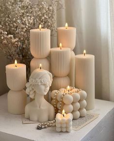 some candles are sitting on a table next to a vase with flowers and pearls in it