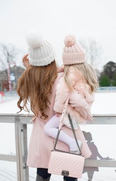 two girls in winter coats and hats, one carrying a pink handbag