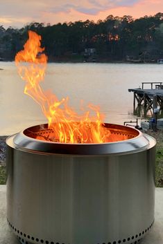 a large metal fire pit sitting on top of a cement slab next to a lake