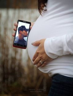 a pregnant woman holding her cell phone to take a photo with her husband's belly