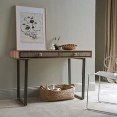 a desk with a basket underneath it next to a chair and painting on the wall