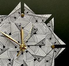 a clock made out of white paper with gold hands and numbers on the face, sitting in front of a black background