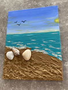 two seashells are on the sand by the ocean with birds flying over it