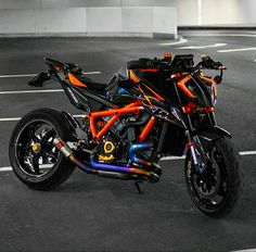 an orange and black motorcycle parked in a parking lot next to a building with lights on