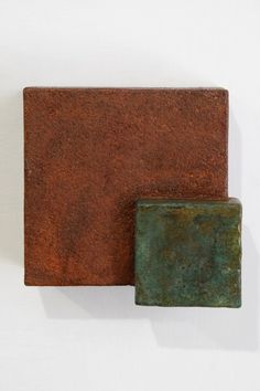 two square pieces of metal sitting on top of each other in front of a white wall