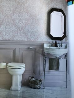 a white toilet sitting next to a sink in a bathroom with wall paper on the walls