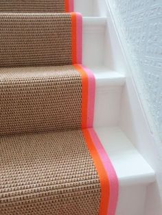 an orange and white striped stair runner on the bottom of a set of beige stairs