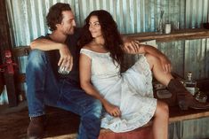 a man sitting next to a woman on top of a wooden bench in front of a metal wall