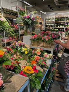 a woman is looking at flowers in a flower shop with lots of potted plants