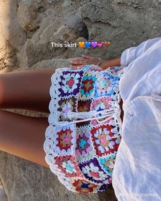 a woman is sitting on the rocks with her hand in her pocket and crocheted shorts