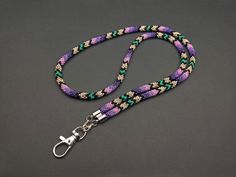 a purple and green lanyard with silver clasps on a gray background, the lanyard has a metal hook