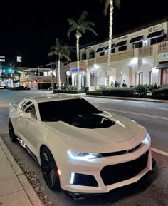 a white chevrolet camaro parked on the side of the road at night with palm trees in the background