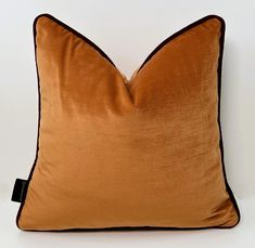 an orange and brown pillow with black piping on the front, sitting against a white wall