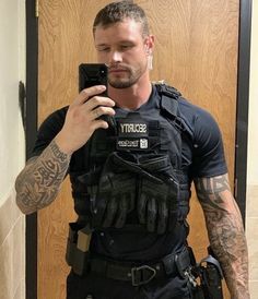 a man with tattoos taking a selfie in the mirror while wearing a security vest