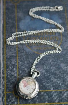 "Silver World Map Pocket Watch Necklace Made with a glass antique map cabochon and silver pocket watch. Carry the world with you! This traveler necklace is created with a real, working pocket watch that measures 1.5x2\" and hangs from a 32\" extra long chain. The pendant is adorned with a high quality antique map print that has been sealed behind a 25mm magnifying glass dome. All jewelry comes packaged in a kraft cotton filled box with an elastic ribbon ready to gift! Note: These necklaces are w Vintage Silver Necklaces For Travel, Vintage Silver Necklace For Travel, Pocket Necklace, Globe Necklace, Gift For Traveler, Map Jewelry, Travel Necklace, Pocket Watch Necklace, Silver Pocket Watch