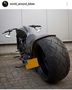 a black motorcycle parked on the side of a road next to a building with white walls