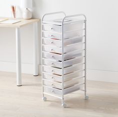 a white cart with lots of drawers on top of it next to a wooden table