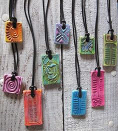 several necklaces with different designs on them hanging from a wooden surface, one is multicolored and the other has black cord