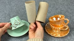 a person holding two rolls of toilet paper next to a cup and saucer