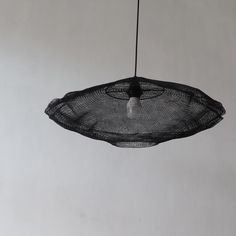 a black netted light hanging from a wire on a white wall with an object in the background