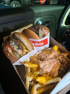 two hamburgers and french fries in a box on the back seat of a car