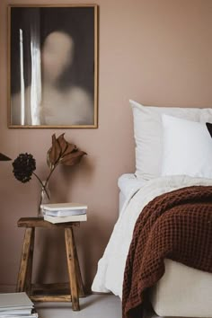 a bedroom with pink walls and white bedding, wooden stools, and a painting on the wall