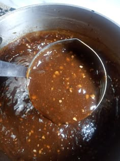 a ladle full of brown sauce being stirred by a metal spoon in a pot