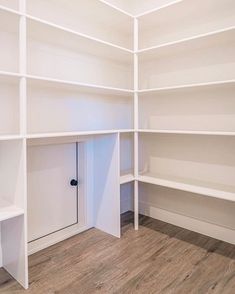 an empty room with white shelving and wood flooring on the walls, in front of a door