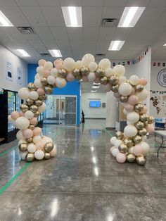 an arch made out of balloons in the middle of a school hallway with tables and chairs