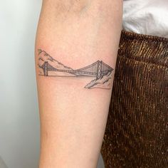 a woman's arm with a tattoo of a bridge and mountains in the background