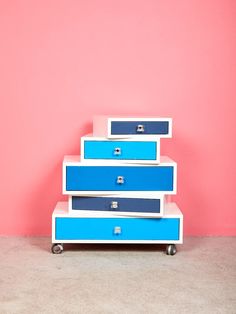 a blue and white dresser sitting in front of a pink wall with drawers on it