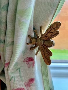 a wooden insect sitting on the side of a window sill next to a flowered curtain