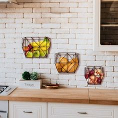 three metal fruit baskets hanging on a white brick wall above a kitchen counter with an oven