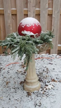 a red ball sitting on top of a white vase filled with pine needles and snow