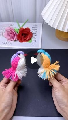 two small birds made out of yarn sitting on top of a table next to a lamp