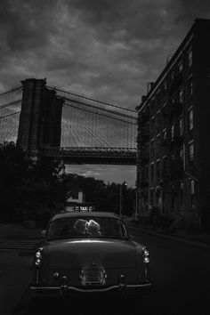 a black and white photo of a car driving down the street in front of a bridge