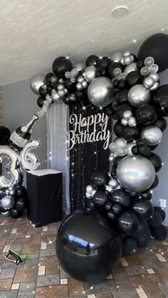 black and silver balloons are arranged in the shape of a happy birthday balloon arch on a tiled floor