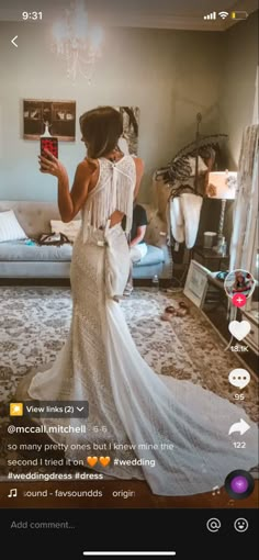 a woman in a white dress taking a selfie with her cell phone while standing in front of a bed