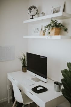 a white desk topped with a computer monitor next to a potted plant on top of it