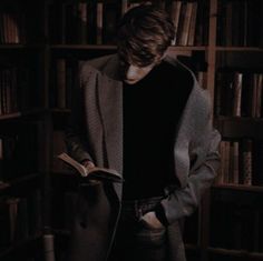 a man standing in front of a book shelf holding an open book and looking at it