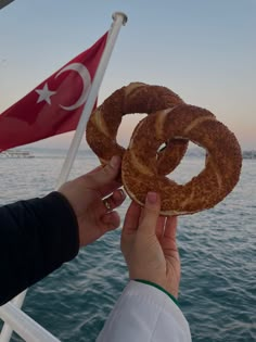 two donuts are being held up to the camera by someone's hand on a boat