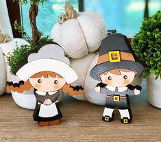 two paper dolls standing next to each other on a wooden table with pumpkins in the background