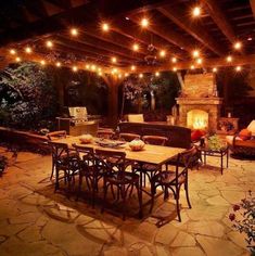 an outdoor dining area with patio furniture and string lights strung over the fire pit at night