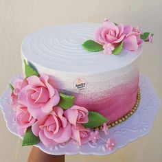 a hand holding a cake with pink flowers on the top and white frosting in the middle