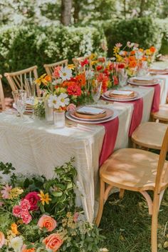 an outdoor table set up with flowers and place settings for the guests to sit at