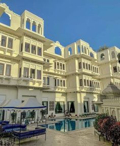 an outdoor swimming pool in front of a large white building with many windows and balconies